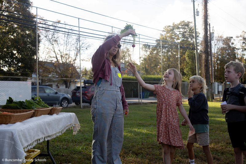 Little girl jumping in the air for a radish that a farmer was holding up. 