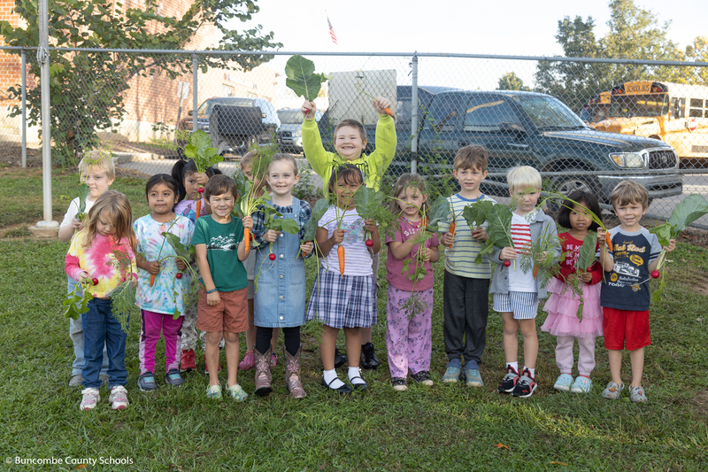 A class of students holding their veggies and smiling at the camera. 