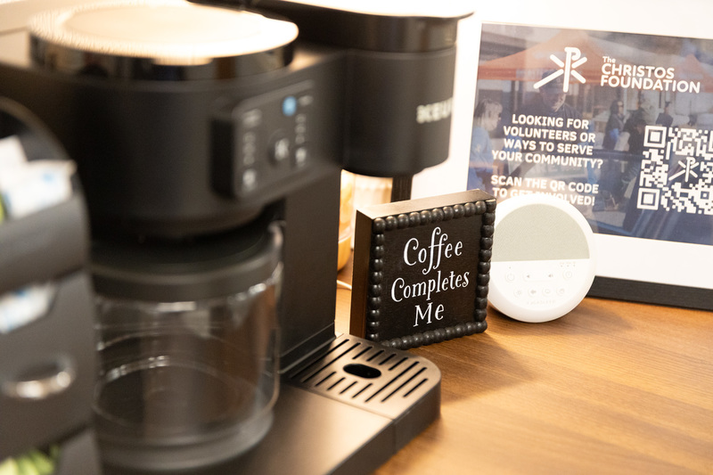A sign next to a Keurig coffee maker that reads "Coffee Completes Me"