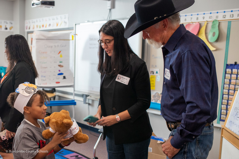 A student wearing a bear handband shows a teddy bear to Mrs. and Mr. Sheppard.