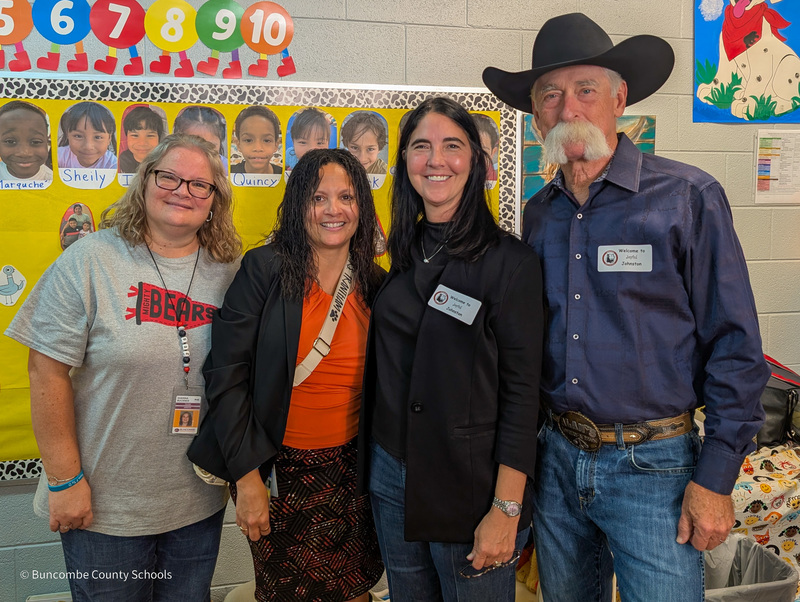 Ms. Buckner, Principal Angie Trantham, Mrs. Sheppard, and Mr. Sheppard post for a photo in front of a classroom bulletin board