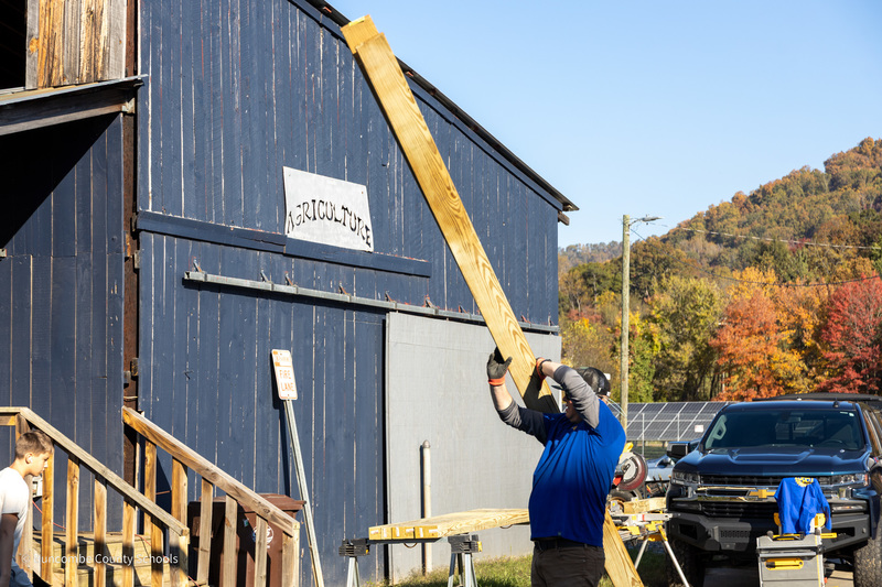 A man carries 2x4's over his shoulder outside the Community High barn.