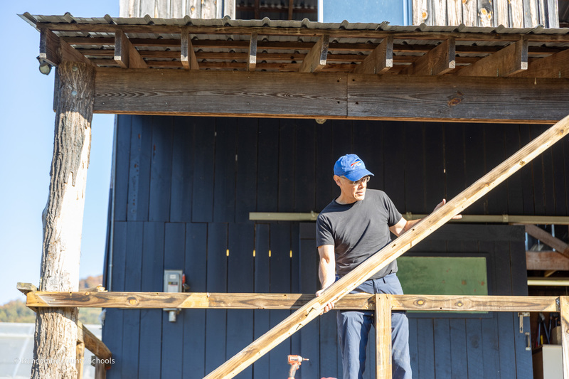 A man stands on the porch of the barn with a 2x4