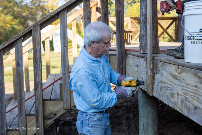 A man uses a drill to loosen a post on the porch of the Community High barn