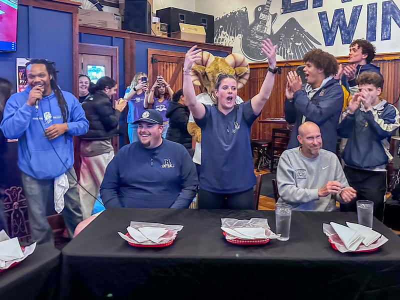 Mrs. Calloway stands up and cheers as she is introduced at the competition. There are people behind her clapping.