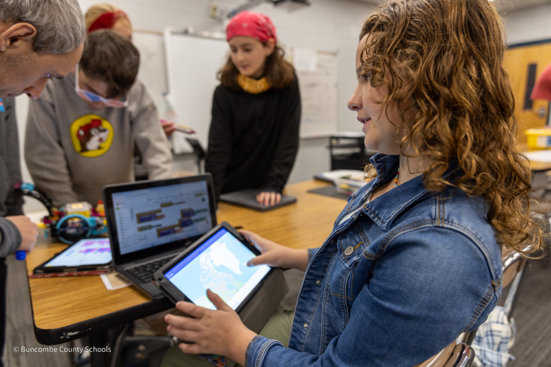 6th grade student Holly shows coding on a laptop while pulling up the app her team created on a tablet.