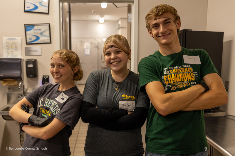 3 Reynolds students pose for a photo in front of the Transformation Village kitchen