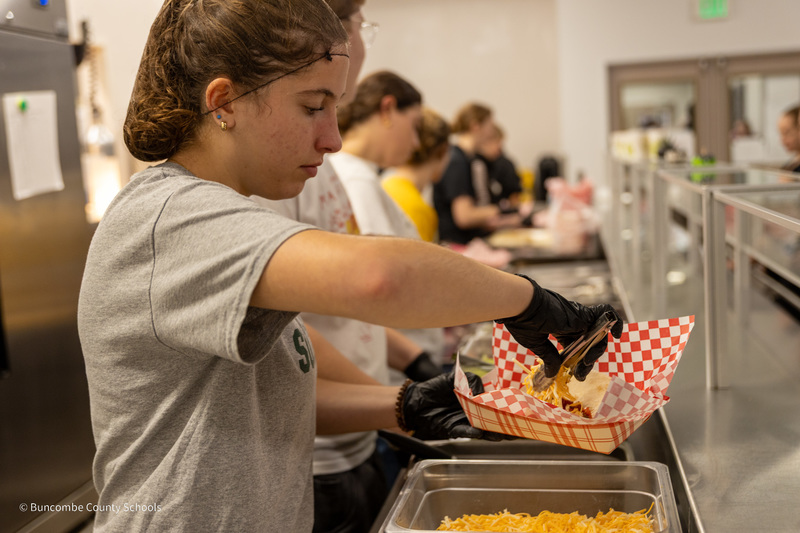 A Reynolds student sprinkles cheese into a soft taco