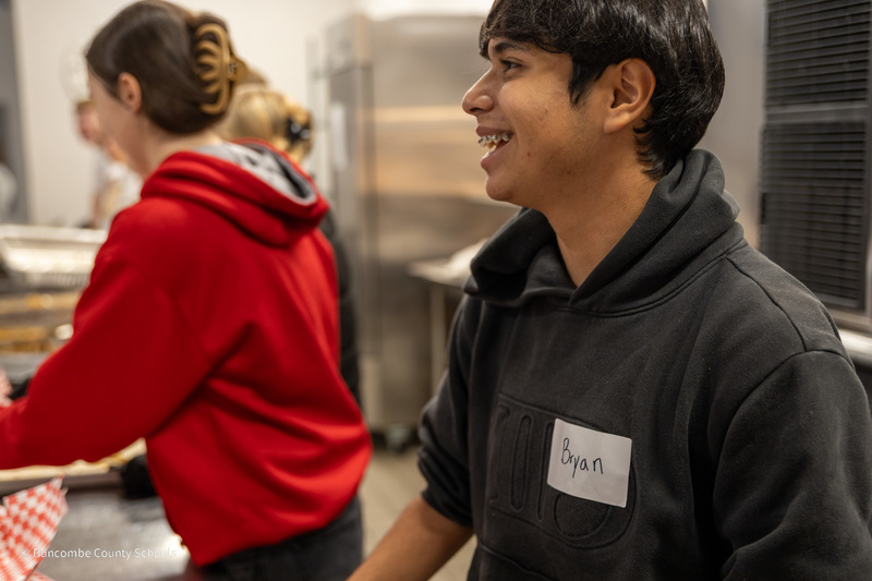 A Reynolds student standing behind the serving line smiles 