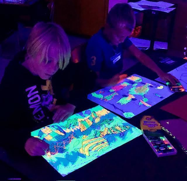 Dark photos of students using fluorescent paint to make an ocean scene under a blacklight.