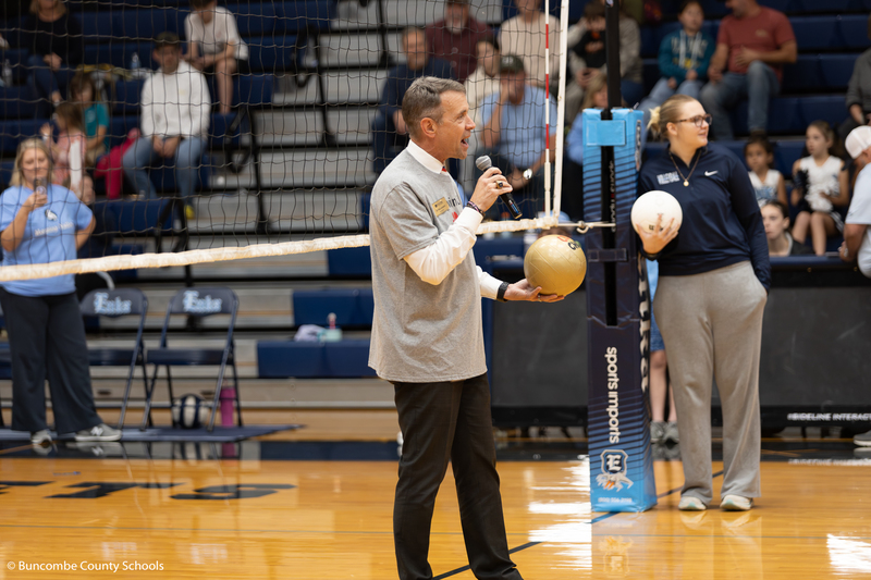Dr. Jackson holding the golden volleyball and talking into the microphone to the crowd at the start of the game.