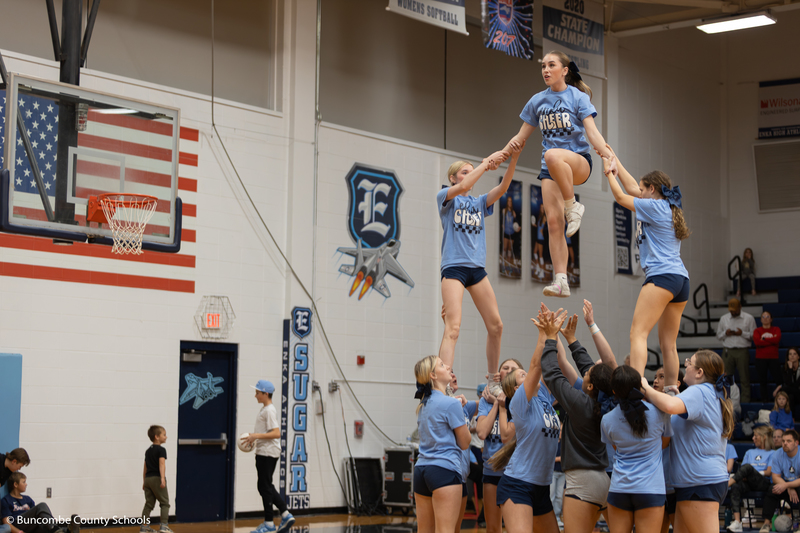 Enka High School cheerleaders doing a stunt on the court. Three cheerleader are in the air.
