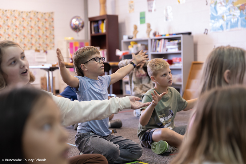 Two boys sitting in the floor with their arms open wide.