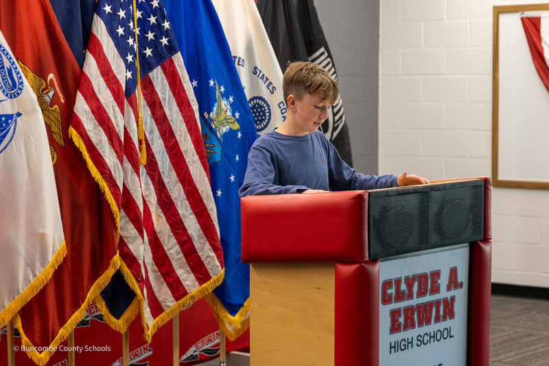 Eblen Intermediate student Boone Davis stands at a podium in front of flags and recites a poem.