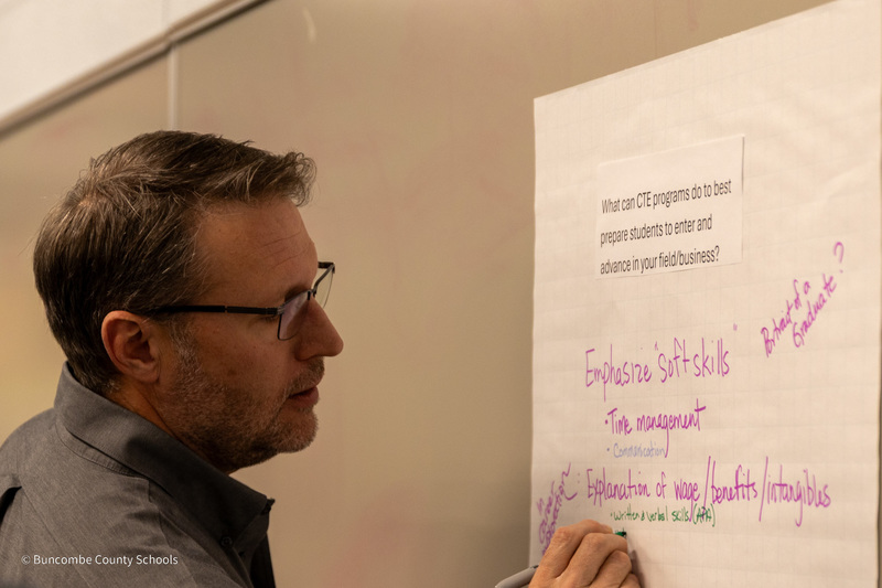 A member of the Business Advisory Council writes on a giant sticky note on the wall.