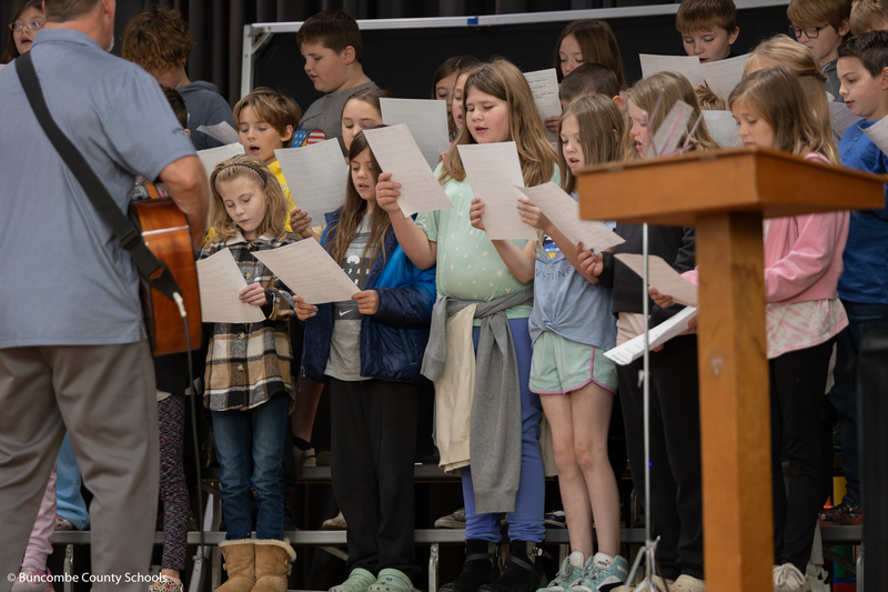Students standing on the stage in the gym singing a song for the veterans. 