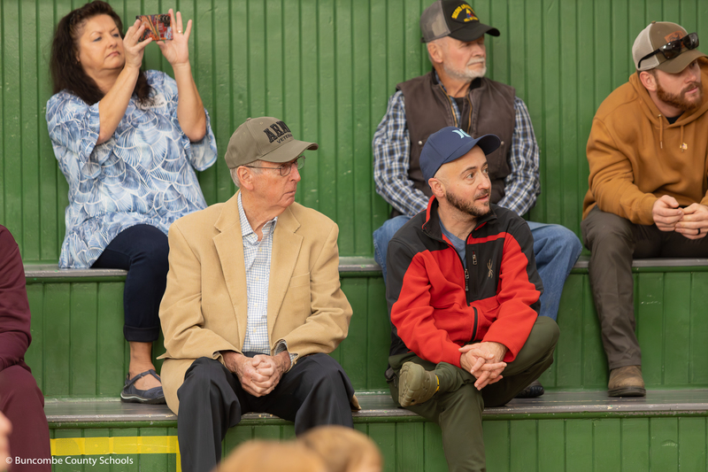 Veterans sitting on the bleachers  enjoying the students singing. 
