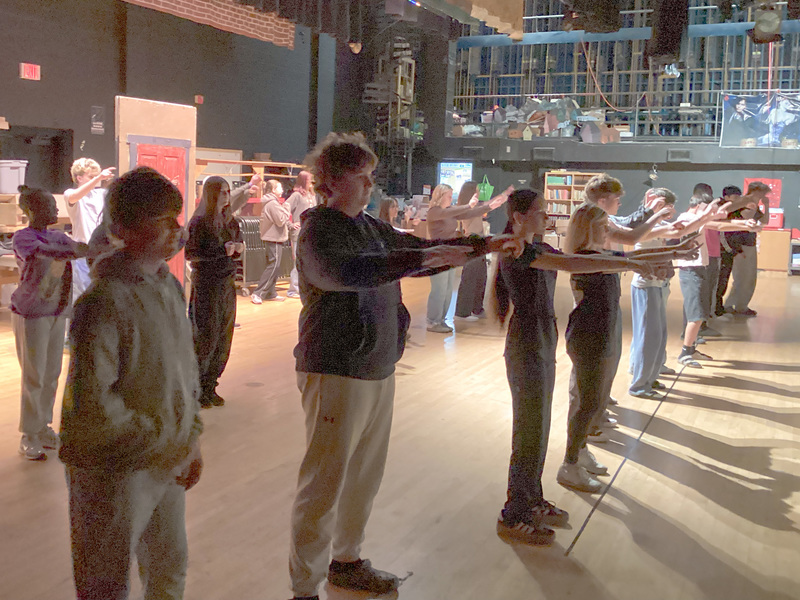 A group of North Buncombe High School students on the stage doing a dance move. They are all  holding out their arms and pointing straight ahead.