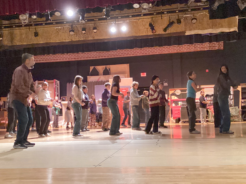 Theater teacher Mr. Webb stands on stage with students preparing to perform a dance.