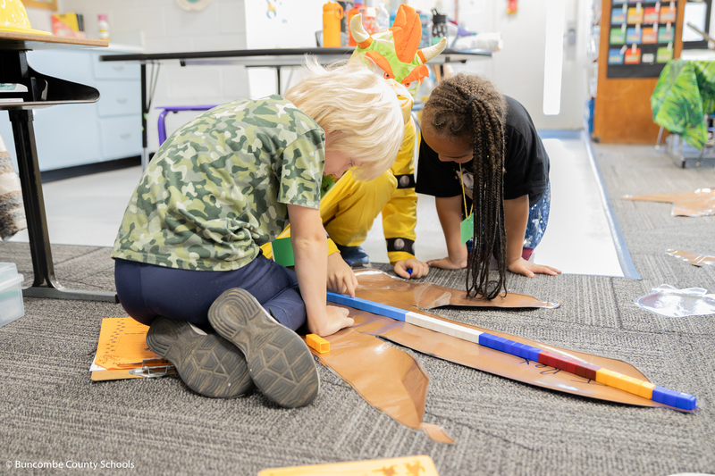 Students using blocks to measure a T-Rex footprint on the floor.