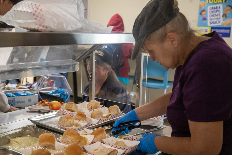 A cafeteria worker puts rolls in individual trays of turkey
