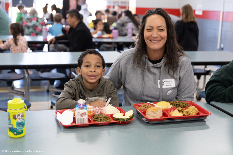 A student and parent sit together in the cafeteria with food trays in front of them.