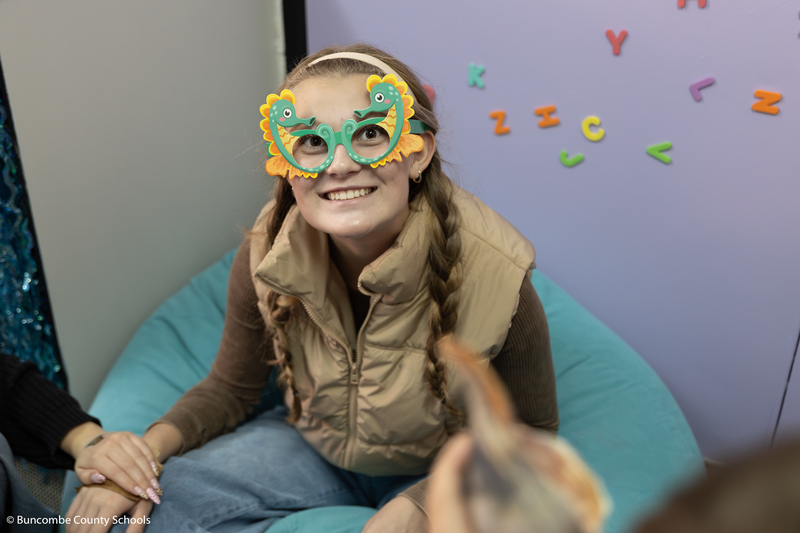 High school student sitting in a bean bag chair, and wearing sea horse glasses and smiling at the camera.