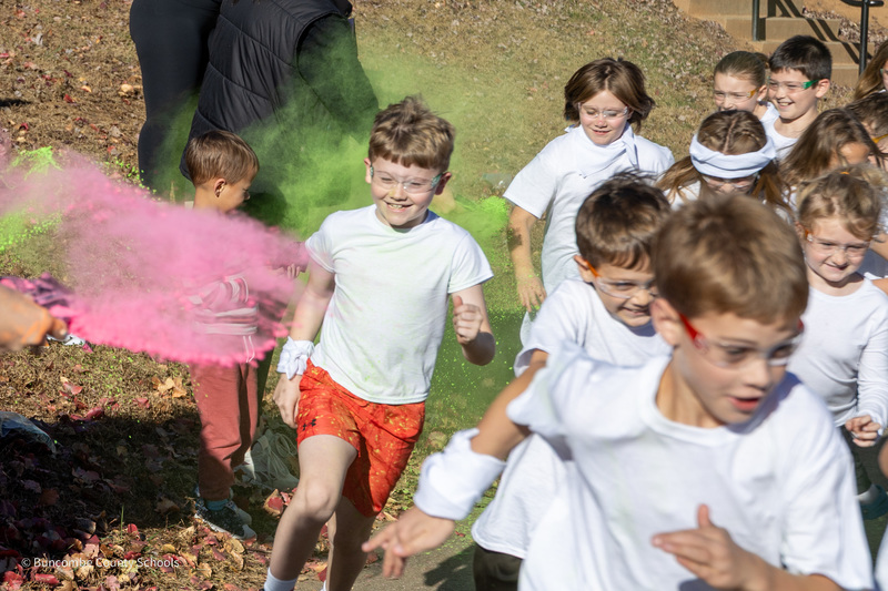 A puff of pink powder floats toward a group of run club members dressed in white t-shirts running around the track