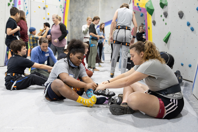 student putting on climbing shoes and harness