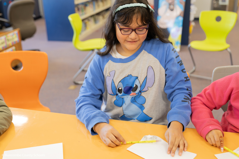 Fourth grade girl wearing blue Stitch shirt looking down smiling at her cartoon flip book she made. 
