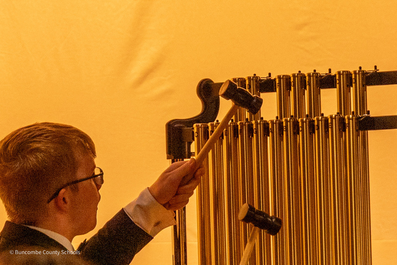 A student holding two mallets plays the chimes