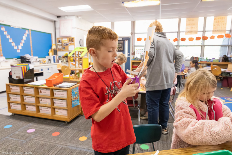 A student cuts a paper bag for a puppet project.