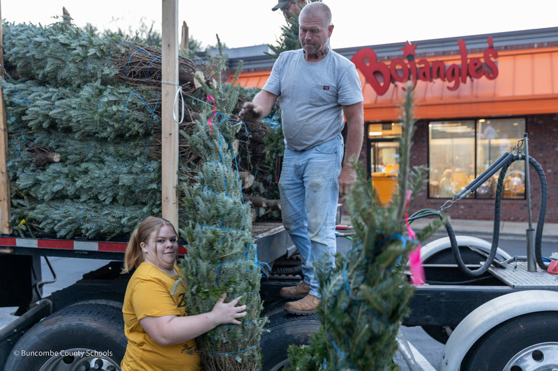 A man standing on the platform truck hands a tree to a student