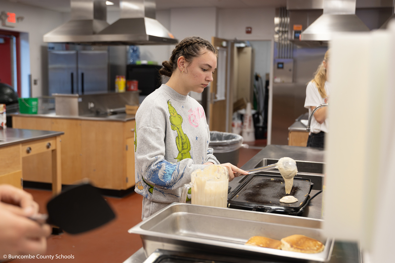 High School girl pouring pancake batter onto a hot griddle. 
