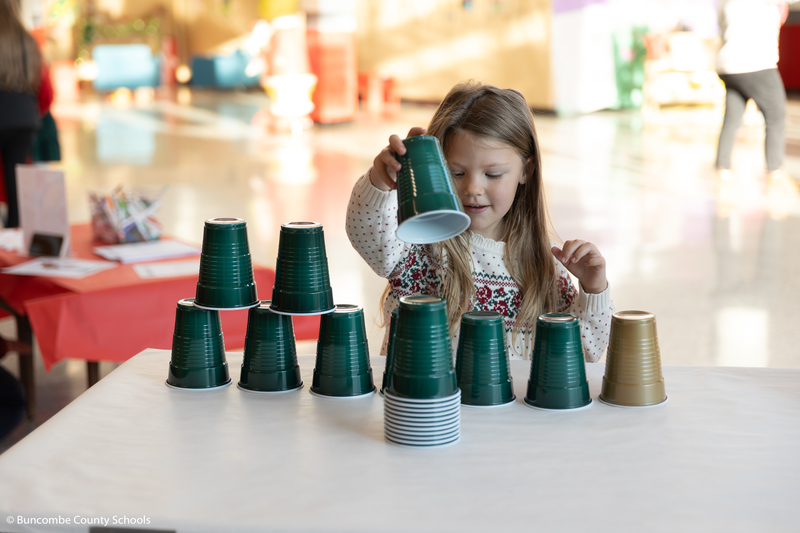 Little girl stacking cups as she builds a Christmas tree out of them. 