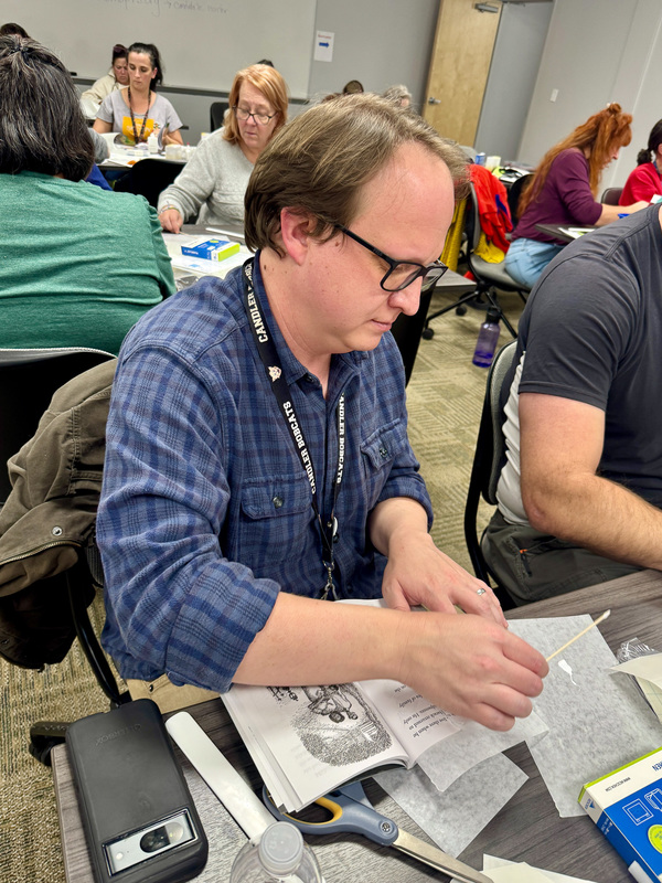 A man uses glue and a cotton swab to repair a  tear in a book page