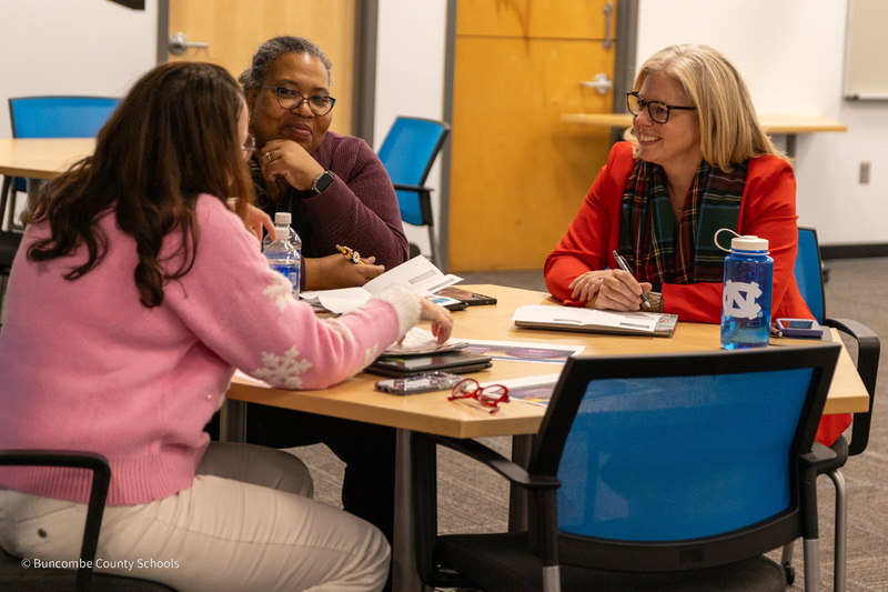 Three people sit at a table and have a small group discussion.