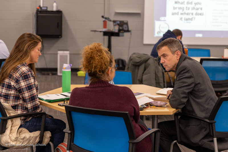 Three people seated at a table have a small group discussion