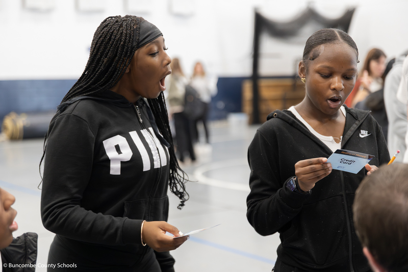 Two girls with shocked expressions on their face, reading what their credit card scenario says.
