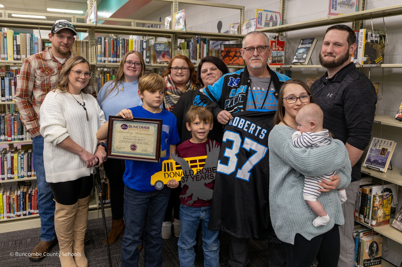Mr. Roberts poses for a photo with his family in front of a media center book shelf.