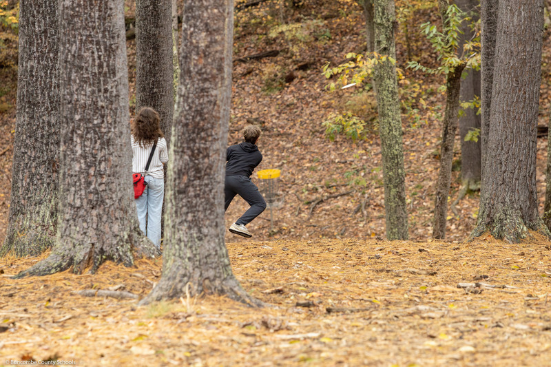 Students play one of the disc golf holes in the woods.