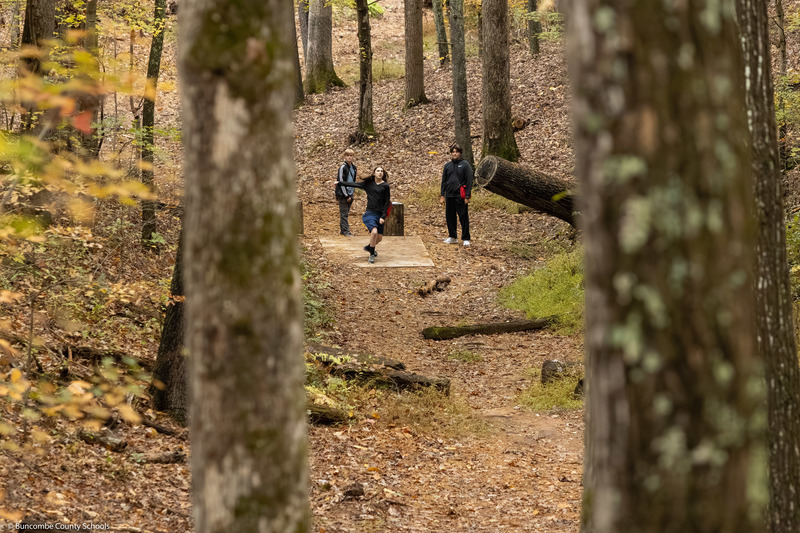 A faraway shot of a student throwing a disc from the tee.