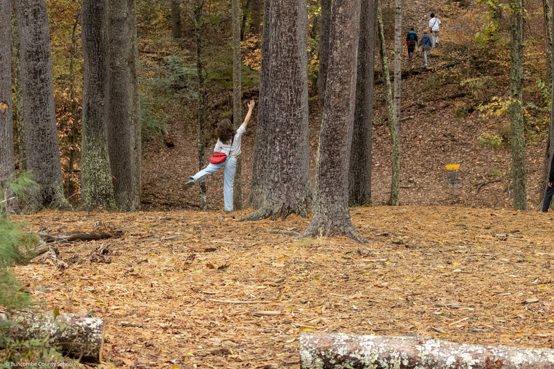 A student plays one of the disc golf holes in the woods.