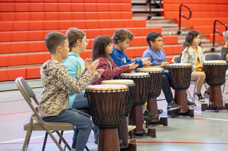 Students play floor drums with their hands.