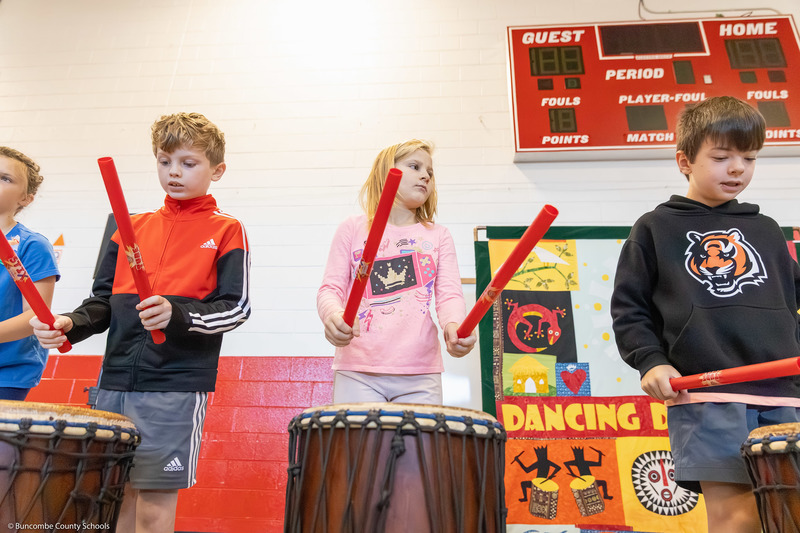 Students use plastic tubes to hit floor drums.