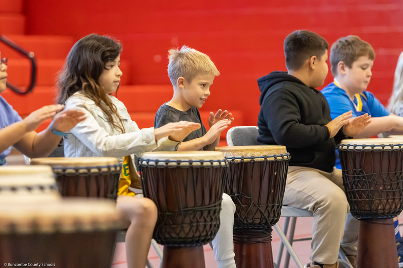 Students play floor drums with their hands.