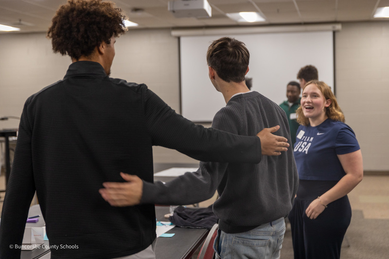 Two students pat each other on the back as a third smiles at them.