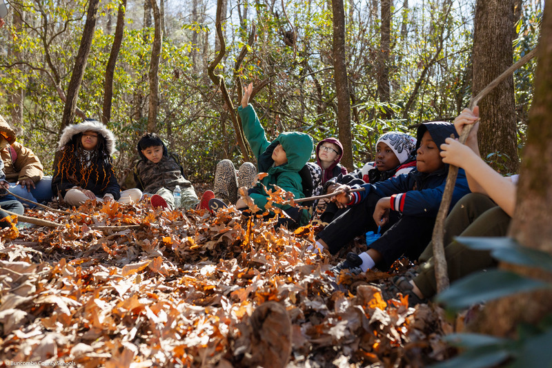 A student asks a question while sitting on the ground with other students.