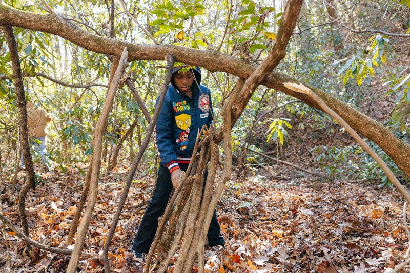 A student works on a shelter in the woods.