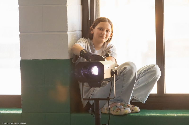 A student smiles behind a spotlight during the dress rehearsal.